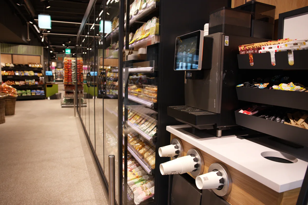 Ein Kühlregal steht an der Seite, vorne eine Kaffeemaschine.